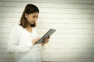 le magnifique asiatique affaires femme est vérification sa de l'entreprise travail sur sa tablette et une sourire sur sa affronter. photo