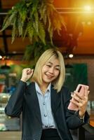 asiatique magnifique affaires femme content avec bien nouvelles sur mobile téléphone dans café. photo