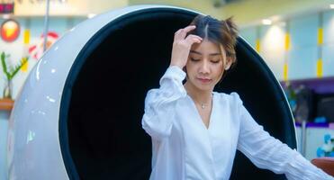 magnifique asiatique affaires femme séance sur une moderne rond chaise émouvant sa cheveux et à la recherche vers le bas, numérique commercialisation. photo