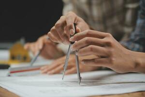 équipe de Multi-éthnique architectes travail sur construction des plans dans réunion chambre. ingénieurs discuter sur projet dans bureau. mature homme d'affaire et femme permanent autour table travail sur plan. photo