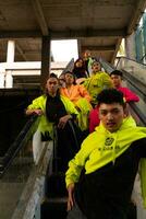 une groupe de asiatique Hommes dans citron vert vestes sont permanent avec leur copains sur le escalier mécanique photo