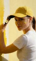 une femme dans une base-ball casquette et travail vêtements les usages une grand peindre brosse à peindre une mur. photo