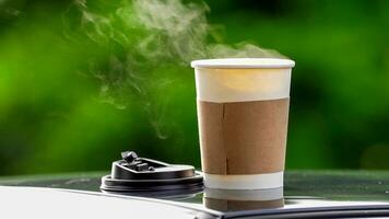 café à emporter dans une papier tasse sur Haut de le voiture toit vert arbre Contexte à lever du soleil dans le matin, sélectif se concentrer, doux se concentrer. photo