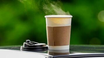 café à emporter dans une papier tasse sur Haut de le voiture toit vert arbre Contexte à lever du soleil dans le matin, sélectif se concentrer, doux se concentrer. photo