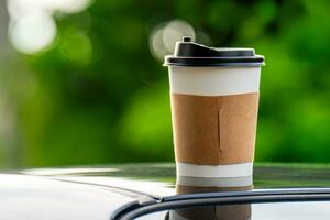 café à emporter dans une papier tasse sur Haut de le voiture toit vert arbre Contexte à lever du soleil dans le matin, sélectif se concentrer, doux se concentrer. photo