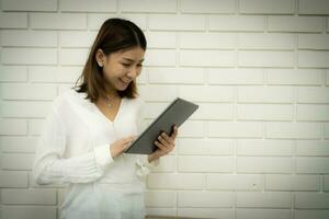 le magnifique asiatique Bureau fille est vérification sa entreprise travail sur sa tablette et une sourire sur sa affronter. photo