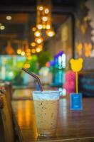 la glace café dans une Plastique tasse sur en bois table avec bokeh Contexte. photo