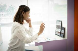 magnifique asiatique en ligne vendeur est salutation le public dans une vivre diffuser tandis que séance dans sa bureau. photo