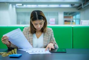 Jeune magnifique asiatique affaires femme est à la recherche vers le bas à financier les documents là sont or pièces de monnaie et une tablette sur une noir tableau. photo