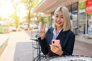 magnifique Jeune femme d'affaires avec détient en haut deux des doigts. le autre main en portant le téléphone elle est très content à faire cette emploi. photo