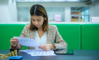 Jeune magnifique asiatique affaires femme est vérification financier documents, avec or pièces de monnaie et une tablette sur le tableau, numérique commercialisation. photo