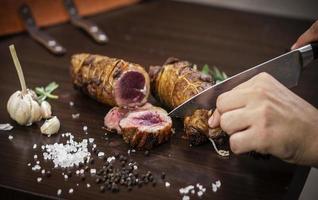 Trancher une portion de rouleau de rosbif biologique avec un couteau sur une table en bois avec du poivre à l'ail et du sel à Melbourne en Australie