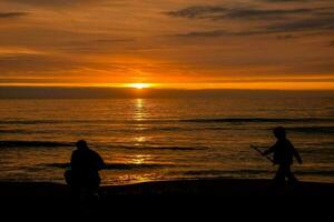 deux gens en marchant sur le plage à le coucher du soleil photo