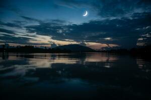 voir le islamique lune dans le nuit ciel. le soir ciel et le vaste rivière dans obscurité sont belle. le croissant lune concept, le symbole de Islam, commence le mois de Ramadan, eid Al fitr photo