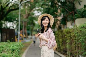 portrait de asiatique Jeune femme voyageur avec tissage chapeau et panier content sourire sur vert Publique parc la nature Contexte. périple voyage mode de vie, monde Voyage explorateur ou Asie été tourisme concept. photo