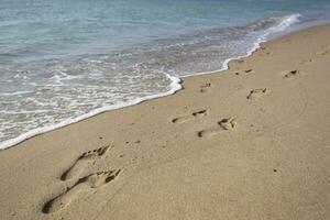 empreintes dans le le sable contre une mer vague photo