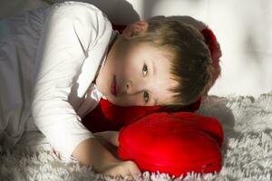 enfant d'âge préscolaire fatigué. le garçon mensonges sur une rouge oreiller photo