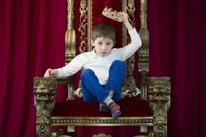 peu garçon dans une couronne dans une luxueux chaise.robe en haut le couronne photo