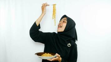 Jeune asiatique femme isolé sur blanc Contexte en portant une assiette de nouilles avec fourchette et en mangeant il photo