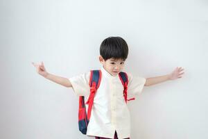 asiatique garçon portant traditionnel thaïlandais vêtements, permanent avec une école sac. faire une faire signe geste en train de préparer à aller à école sur une blanc Contexte photo