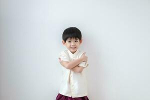 asiatique garçon portant traditionnel thaïlandais vêtements, permanent avec bras franchi. sur une blanc Contexte photo