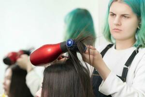 coiffeur séchage brunette cheveux avec rouge cheveux séchoir, bleu brosse à cheveux dans beauté salon photo