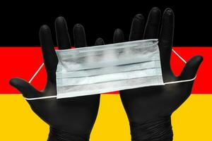 médecin détient visage masque dans mains dans noir médical gants sur Contexte couleurs drapeau de Allemagne ou allemand drapeau. pandémie Assurance coronavirus photo