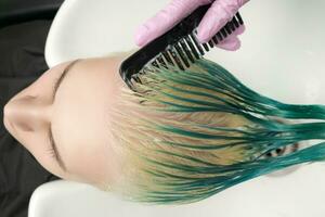 Haut vue de coiffeur en portant humide cheveux dans main et ratissage client longue vert et décoloré cheveux tandis que shampooing dans douche photo