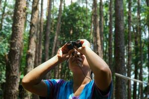 Jeune femme à la recherche à des oiseaux dans le forêt par jumelles. femelle touristique avec outil en train de regarder le la nature dans forêt. en bonne santé mode de vie et éco-tourisme. photo