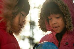 deux jolies filles asiatiques apprennent un modèle du monde sur fond de nature et la lumière du soleil chaude dans le parc. les enfants apprennent à travers des activités ludiques éducatives. Jour de la Terre. journée mondiale de l'environnement. photo