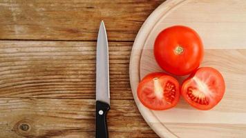 trancher la tomate sur une planche à découper en bois. couteau et tomates sur bois photo
