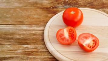 tomate entière et coupée sur une planche en bois pour trancher