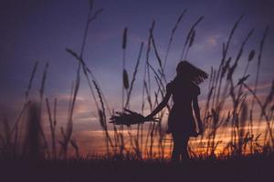 silhouette d'une fille dans un pré sur fond de coucher de soleil photo