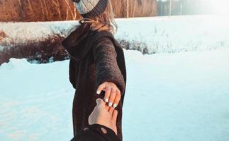 suivez-moi fille tenant la main de son petit ami dans la forêt de neige d'hiver. photo