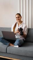 Happy young woman with photo camera using laptop at home