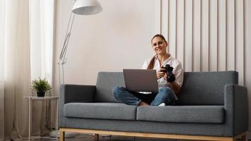 Happy young woman with photo camera using laptop at home