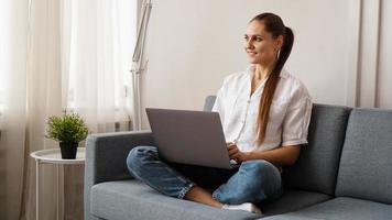 femme heureuse souriante assise sur le canapé et utilisant un ordinateur portable