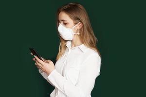 fille dans un masque médical avec téléphone en mains sur fond vert photo