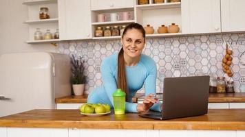 femme souriante utilisant un ordinateur dans une cuisine moderne