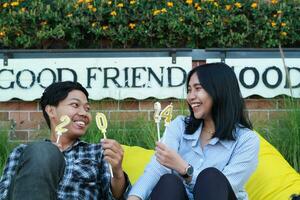 content asiatique couple adolescent à la recherche à chaque autre en portant 20 24 étincelant bougie et séance sur Jaune haricot sac dans maison Cour Prairie avec fleur Contexte dans le soir célébrer Nouveau année photo