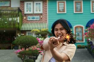 Nouveau année veille fête concept. attrayant asiatique Jeune femme en portant cierge magique avec en riant content dans Extérieur jardin de ancien maison Cour photo