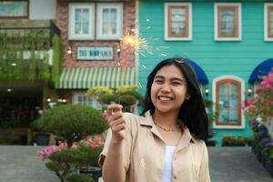 portrait de magnifique content Jeune asiatique femme en portant cierges magiques feux d'artifice à célébrer Nouveau année veille avec jardin fête permanent dans Extérieur ancien maison Cour photo