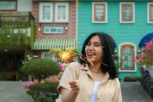 portrait de magnifique content Jeune asiatique femme en portant cierges magiques feux d'artifice à célébrer Nouveau année veille avec jardin fête permanent dans Extérieur ancien maison Cour photo