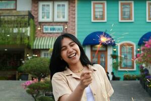 portrait de magnifique content Jeune asiatique femme en portant cierges magiques feux d'artifice à célébrer Nouveau année veille avec jardin fête permanent dans Extérieur ancien maison Cour photo