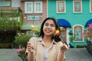 de bonne humeur Jeune asiatique femme en portant cierge magique à célébrer Nouveau année veille avec jardin fête permanent plus de coloré ancien maison Cour photo