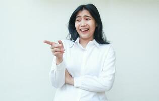 jolie marrant asiatique affaires femme en riant montrer du doigt doigt avec plié bras portant blanc costume chemise permanent plus de isolé Contexte photo