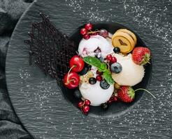 vanille la glace crème boules avec Frais baies sur noir assiette photo