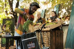 Jeune africain livraison gars en mettant Frais biologique produire dans thermo sac, prise en dehors commande de Les agriculteurs marché. livrer en bonne santé localement grandi des fruits et des légumes à les clients de ferme à seuil de porte photo