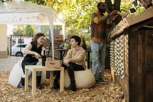 équipe de femmes à nourriture Festival profiter du vin dégustation, séance suivant à local Les agriculteurs marché dehors. client et vendeur en buvant Frais Naturel bouteille de biologique vin, fait maison des produits. photo