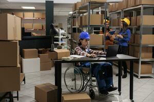 Jeune asiatique entrepôt employé avec physique invalidité gérant livraison opérations sur portable. cargaison Distribution centre ouvrier dans fauteuil roulant Faire bureau travail dans entrepôt photo